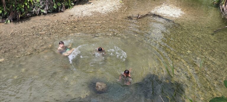 Tour guest child playing and bathing in a clean Siberut rainforest river alongside a Mentawai Sikerei family