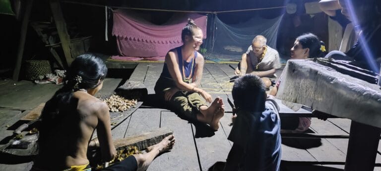 Tour guest joining an evening gathering with a Sikerei family eating forest snails in Siberut