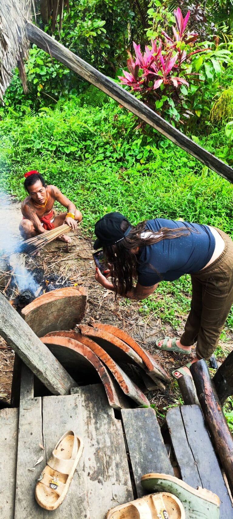 Tour guest photographing a Mentawai Sikerei by the fire inside a Siberut uma