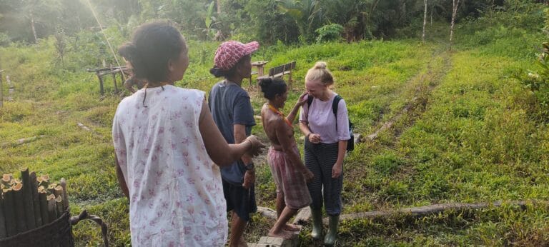Tour guest walking with Mentawai women through a village garden in Siberut