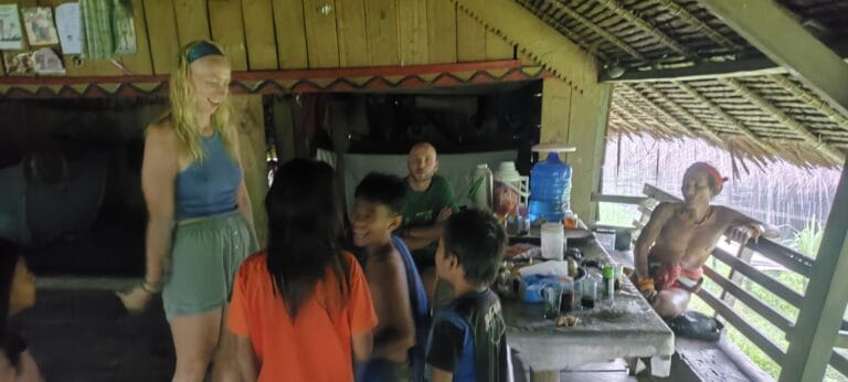 Tour guest with local children and a Mentawai Sikerei inside a traditional uma in Siberut