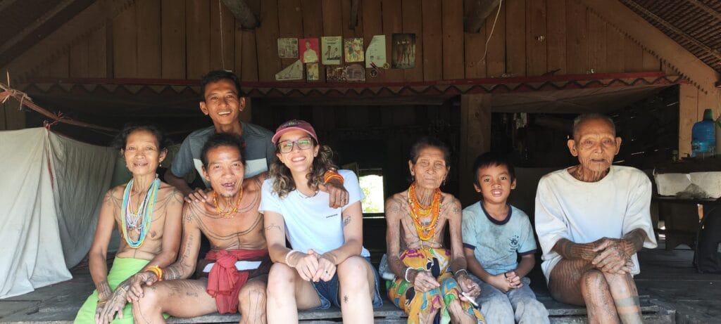 Tour guest posing with the extended Sikerei family inside a traditional uma in Siberut