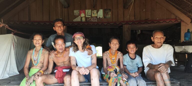 Tour guest posing with the extended Sikerei family inside a traditional uma in Siberut
