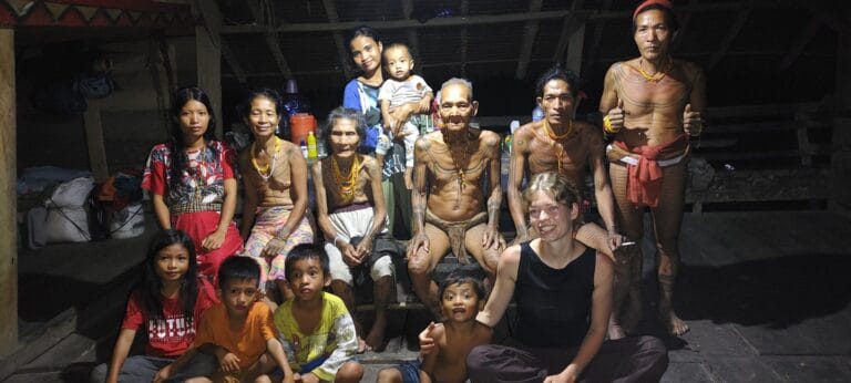 Tour guest posing in a group portrait with a Mentawai Sikerei family in Siberut