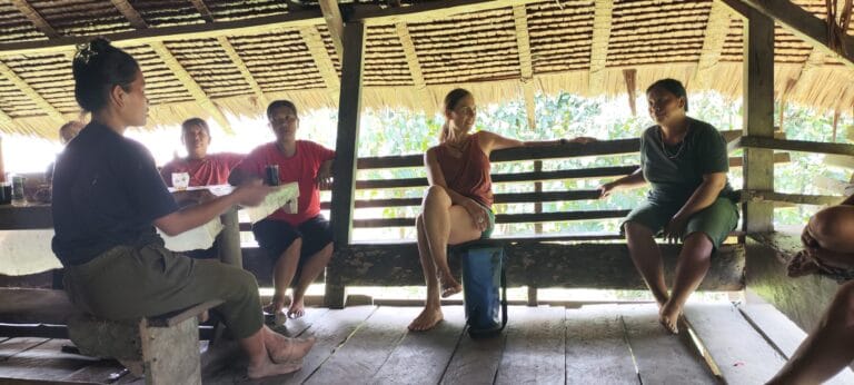 Tour guests conversing with a visiting Mentawai Sikerei inside a traditional Siberut longhouse