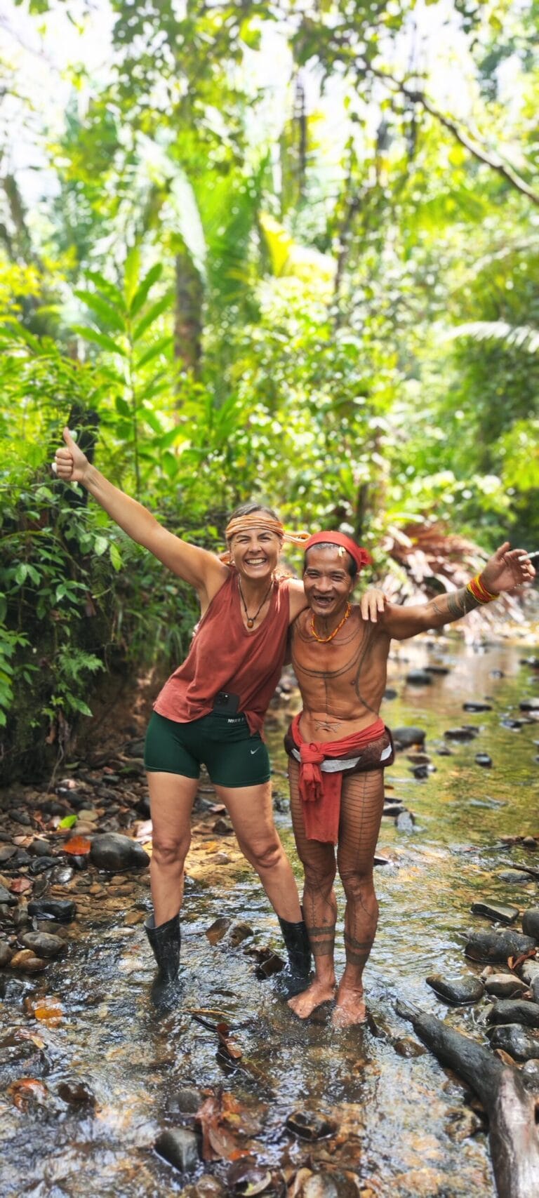 Tour guests hugging and laughing with a Mentawai Sikerei after completing traditional tree bark clothing in Siberut