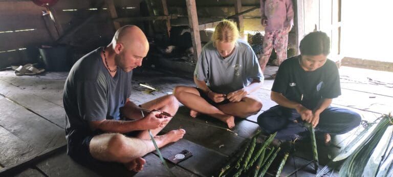 Tour guests learning palm leaf weaving from a Mentawai family in Siberut