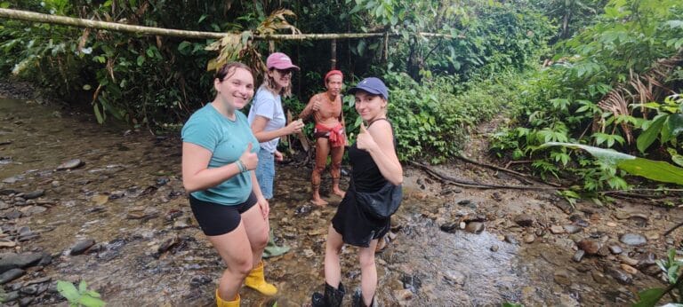 Group of tour guests giving thumbs up with a Mentawai Sikerei standing in the river in Siberut