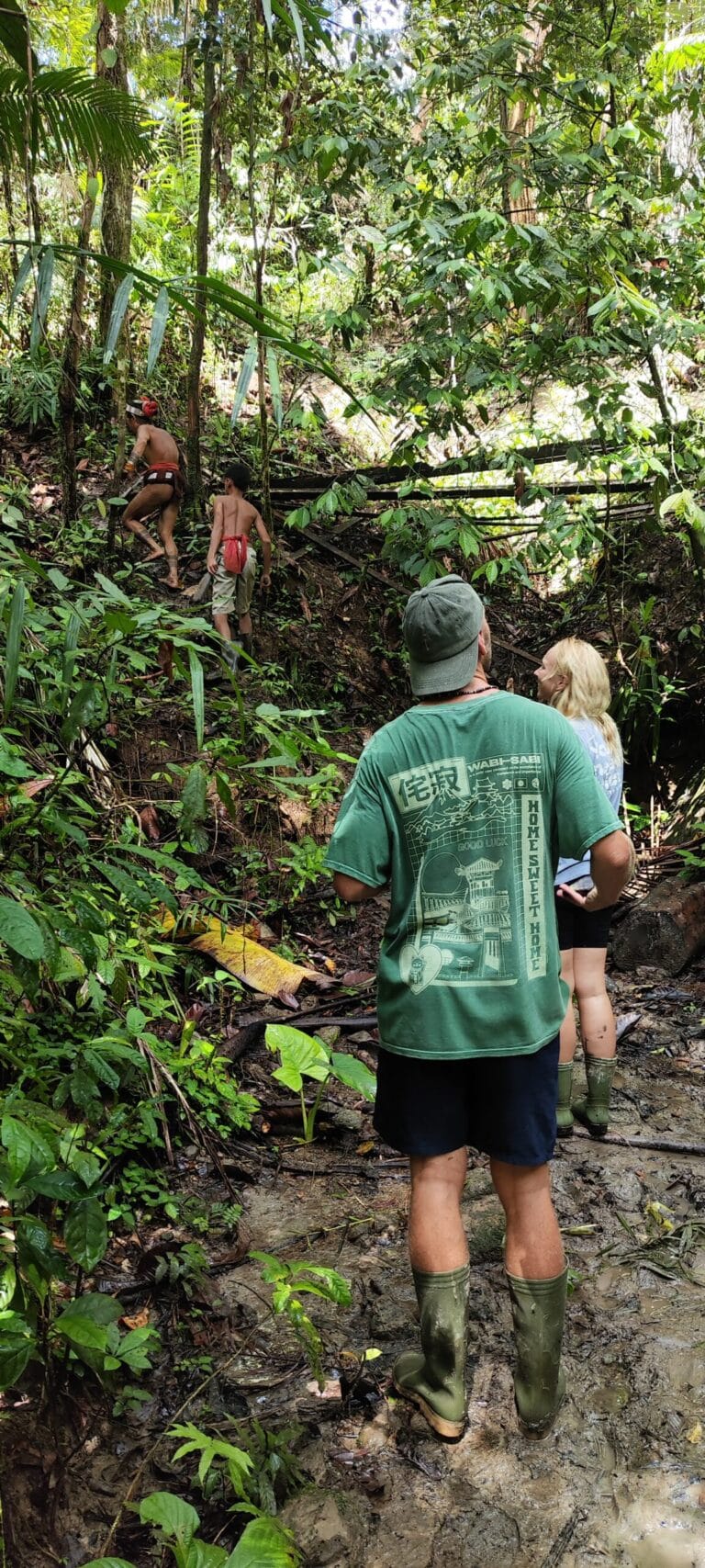 Tour guests trekking a muddy jungle trail alongside a Mentawai Sikerei in Siberut