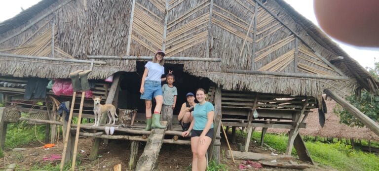 Tour guests with a local boy and village dog at a traditional uma in Siberut