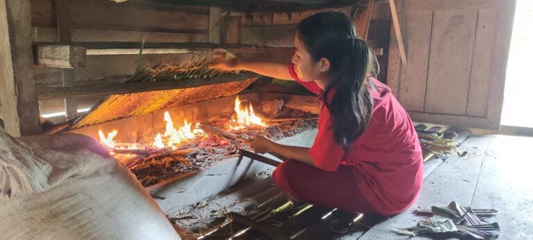 Local Mentawai girl tending a traditional cooking fire inside a Siberut village home