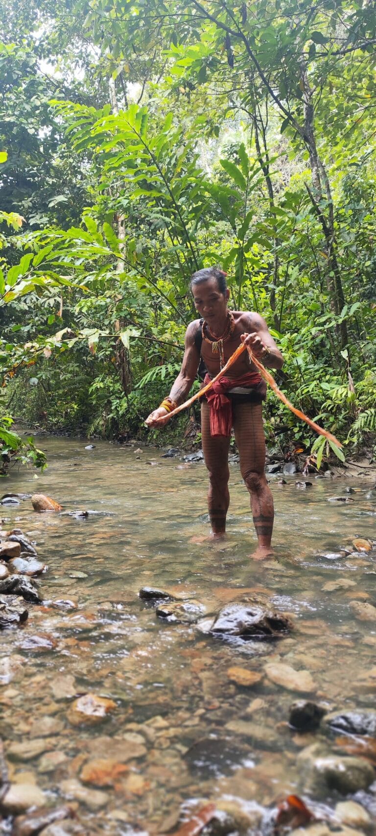 Mentawai Sikerei and tour guest washing newly made traditional tree bark cloth in a Siberut river
