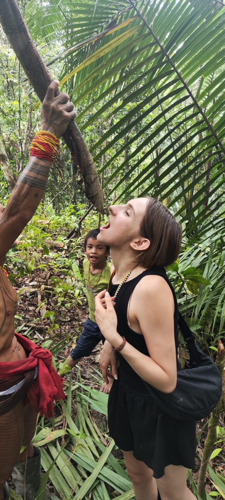 Mentawai Sikerei holding a jungle vine for a tour guest to drink emergency water from, child watching in Siberut