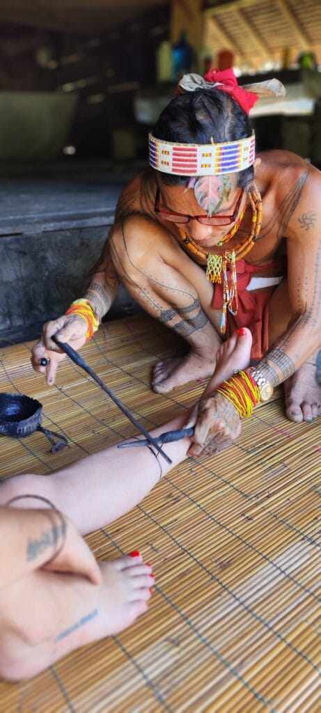 Close-up of a Mentawai Sikerei hand-tap tattooing a tour guest's leg in Siberut
