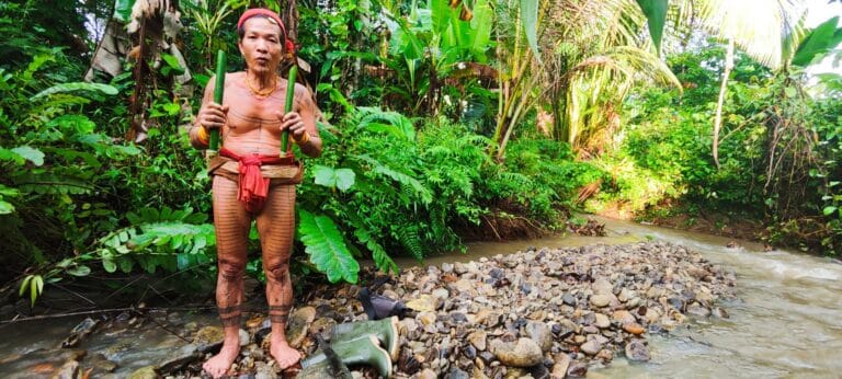 Mentawai Sikerei holding bamboo containers of freshly prepared medicine by a Siberut river