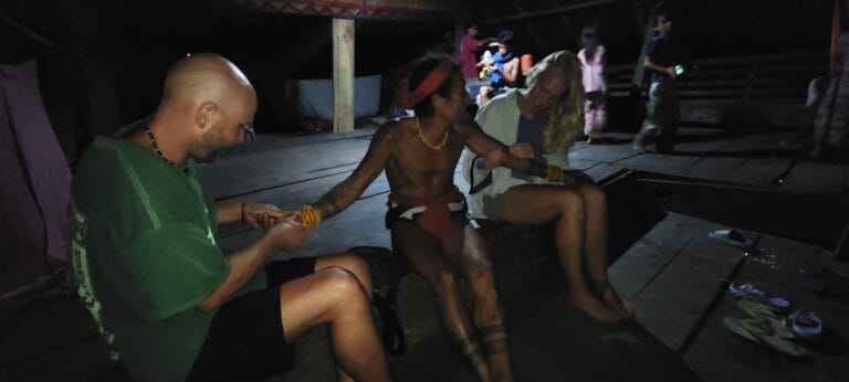 Mentawai Sikerei and tour guests gathered together at night inside a Siberut uma