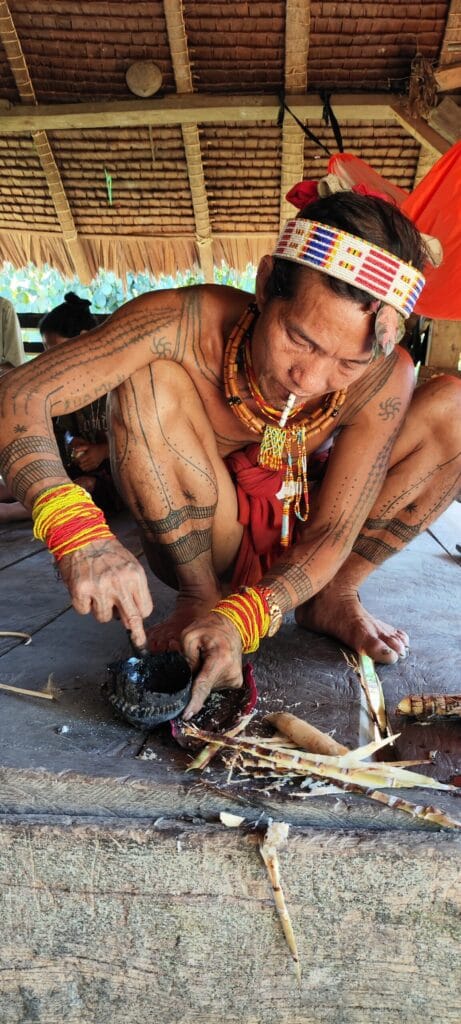 Mentawai Sikerei mixing traditional soot-based tattoo ink in a coconut shell mortar in Siberut