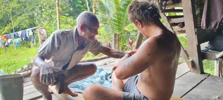 Mentawai Sikerei hand-tap tattooing a tour guest's arm using traditional method in Siberut