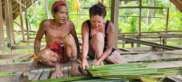 Mentawai Sikerei teaching a tour guest how to weave palm leaves in Siberut
