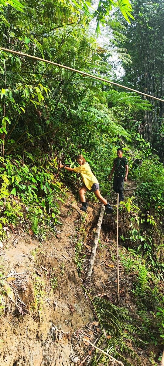 Guest and guide navigating a steep muddy jungle trail, Mentawai