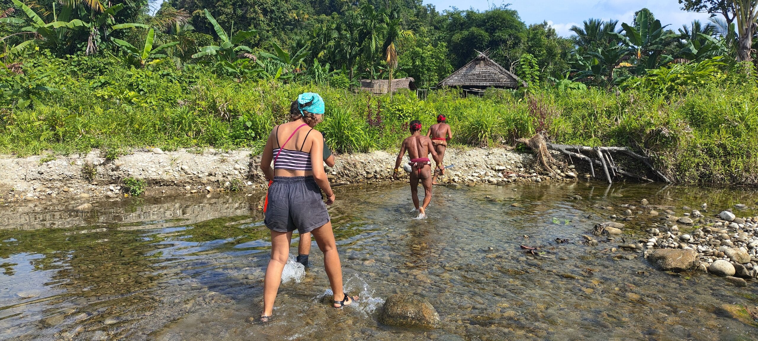Tour guest crossing a river with Mentawai Sikerei men on the way to a Siberut village