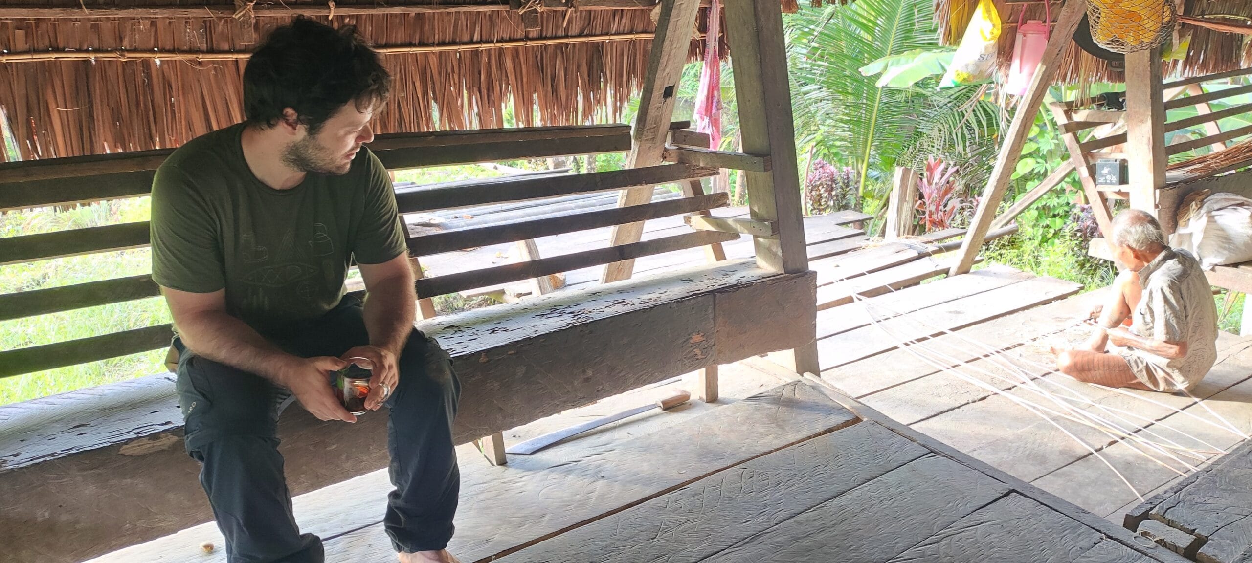 Tour guest sitting with a Mentawai elder on the porch of a Siberut uma longhouse
