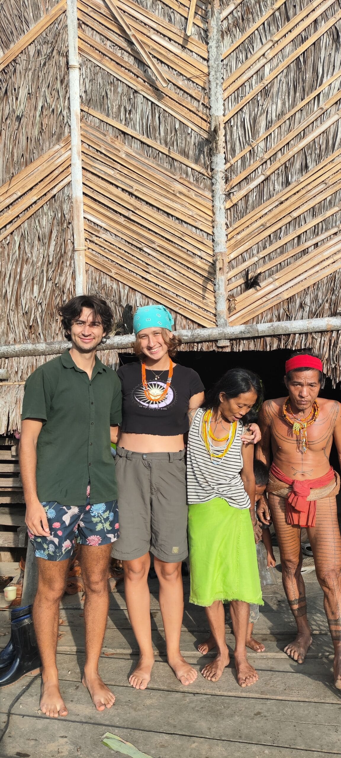 Tour guests group portrait with a tattooed Mentawai Sikerei family inside a Siberut uma