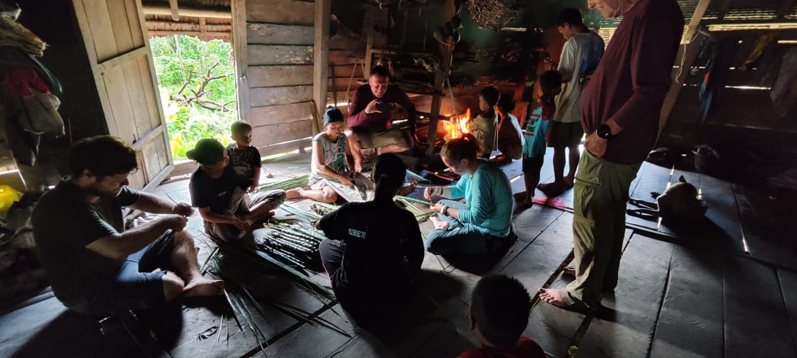 Guests group weaving palm leaves with local children inside Uma