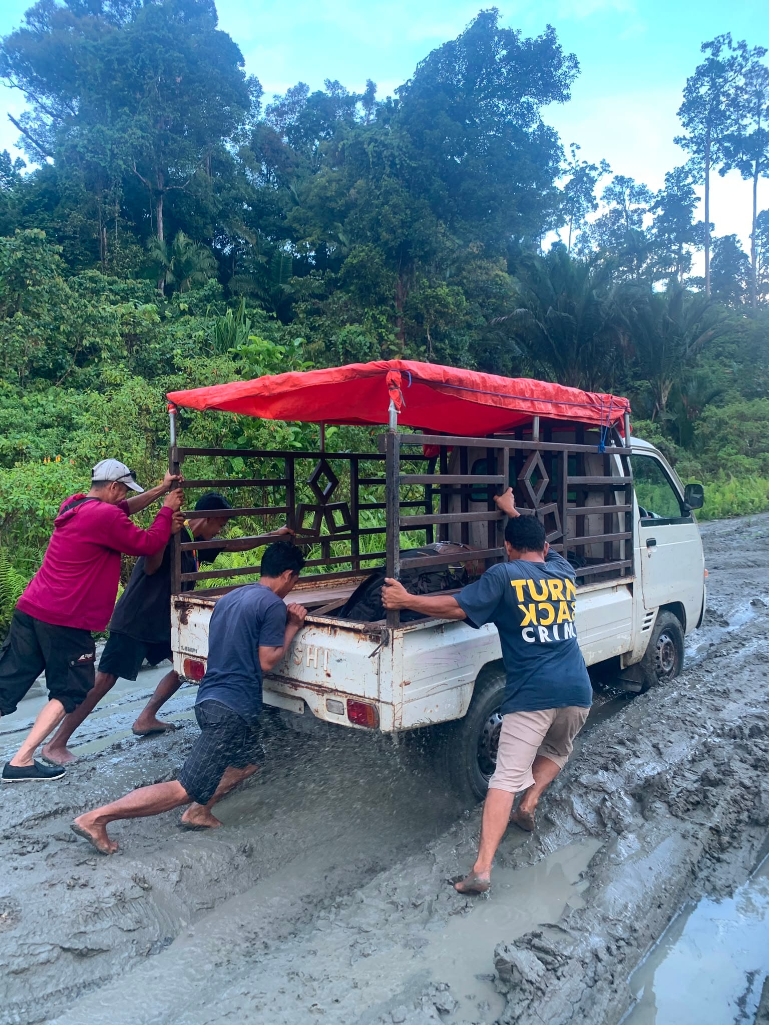 Guides pushing a truck stuck in mud on the Trans-Mentawai road
