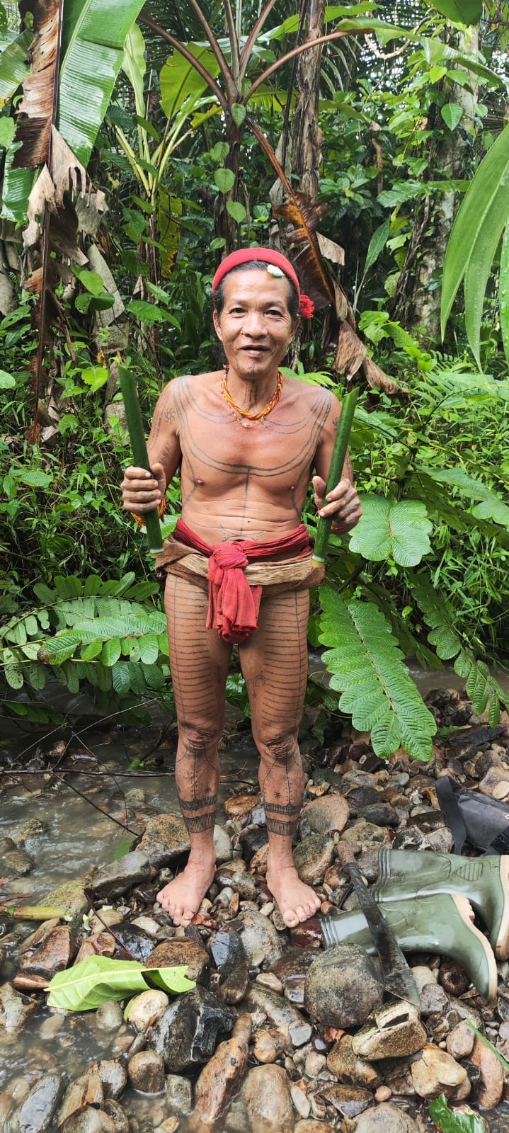 Sikerei in traditional kabit dress with full body tattoos, standing in a river
